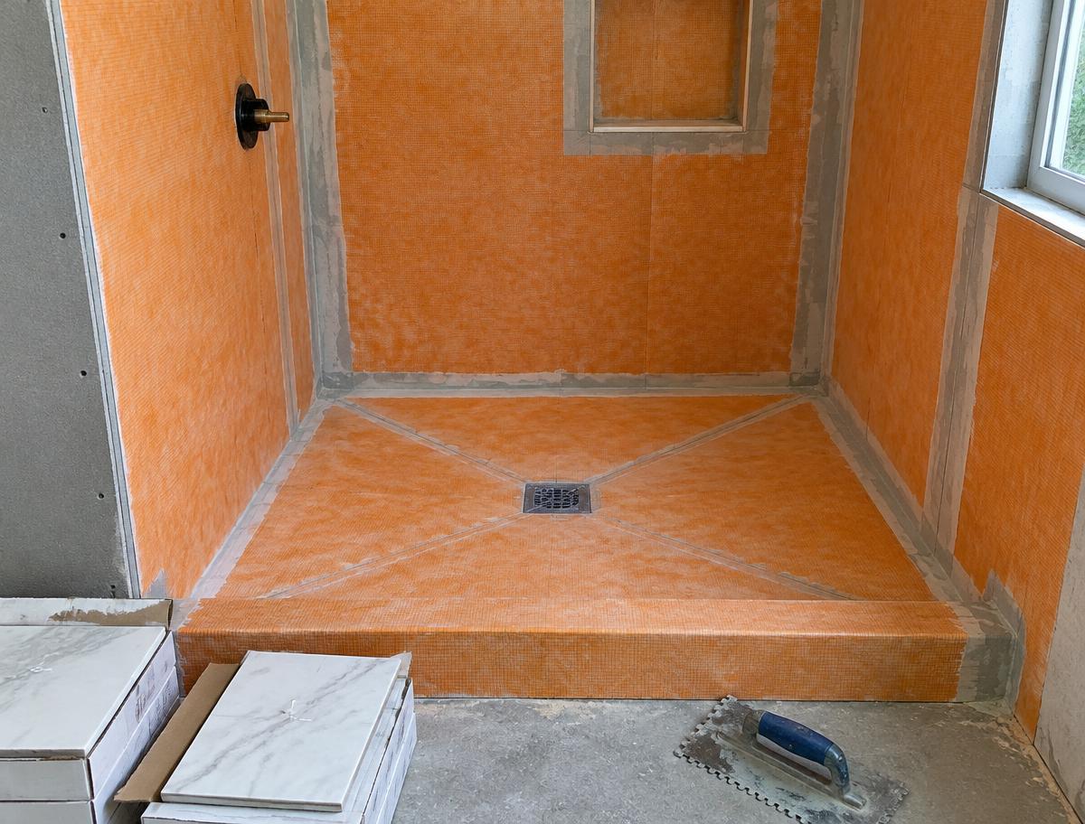 Shower under construction with orange waterproofing membrane on walls and a sloped floor around the drain